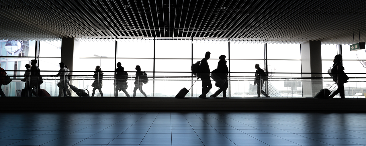 Em um aeroporto, pessoas caminham em direções diferentes carregando malas