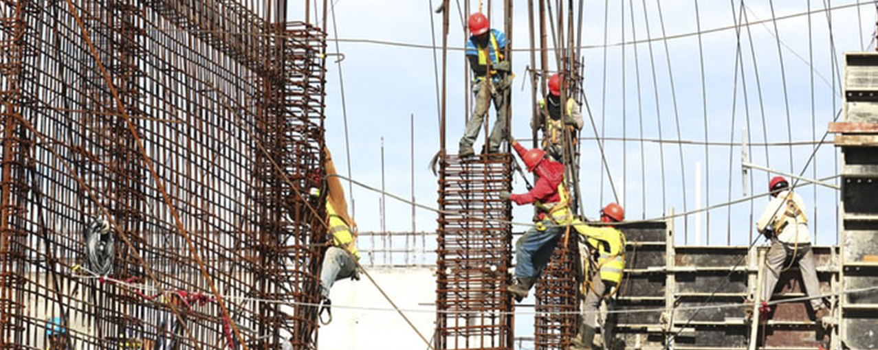 A imagem mostra homens, com equipamentos de segurança, trabalhando na construção de um edifício